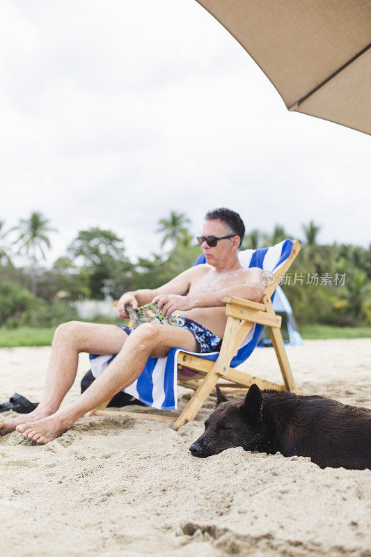 一个带着狗在沙滩上看书的成熟男人
