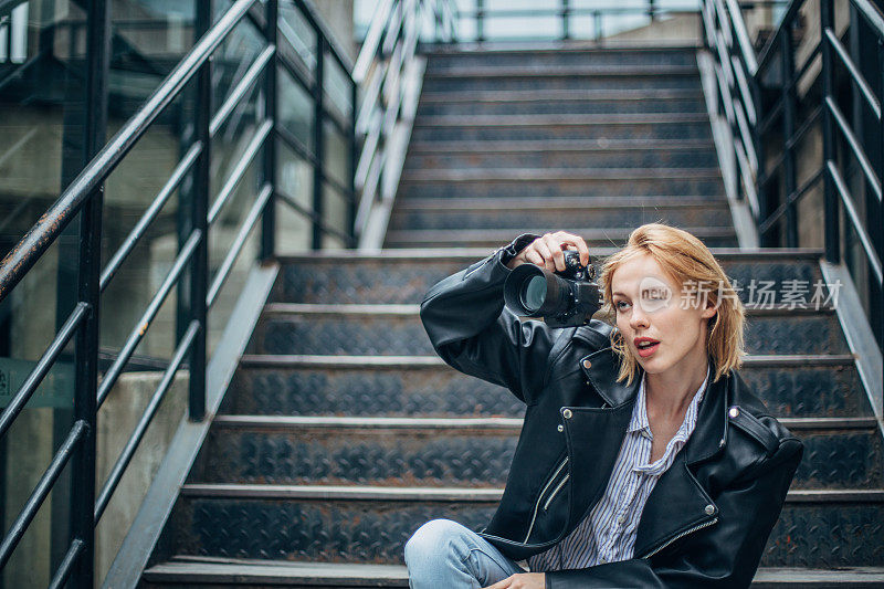 金发女摄影师坐在城市的台阶上