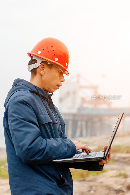一名工程师站在码头前，用一台笔记本电脑指挥工作