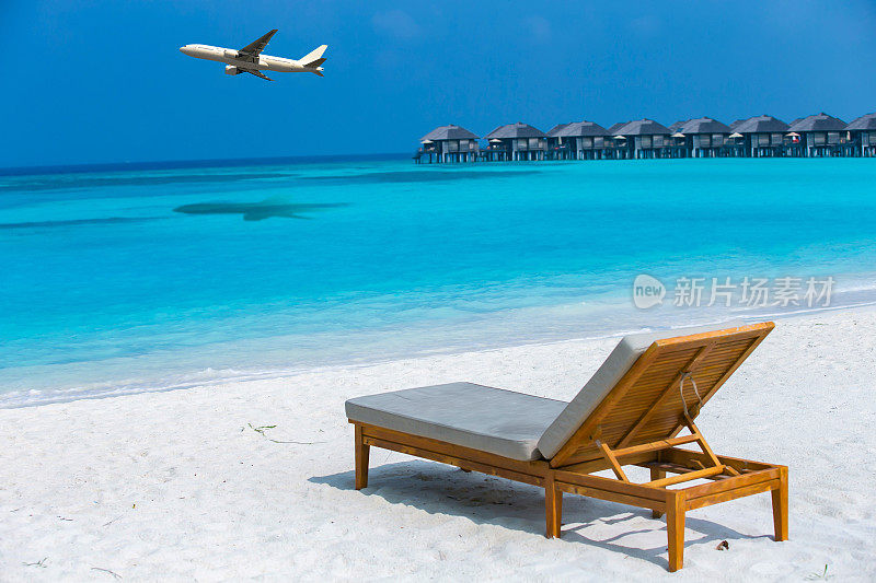 拍摄一架白色飞机飞过热带海域，那里有沙滩、水上别墅和沙滩床