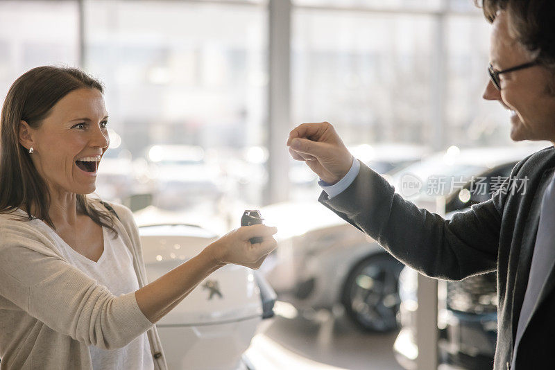 一名女顾客从一名男车商那里拿到新车钥匙后，露出了露齿的笑容，两人在车行室内面面相觑