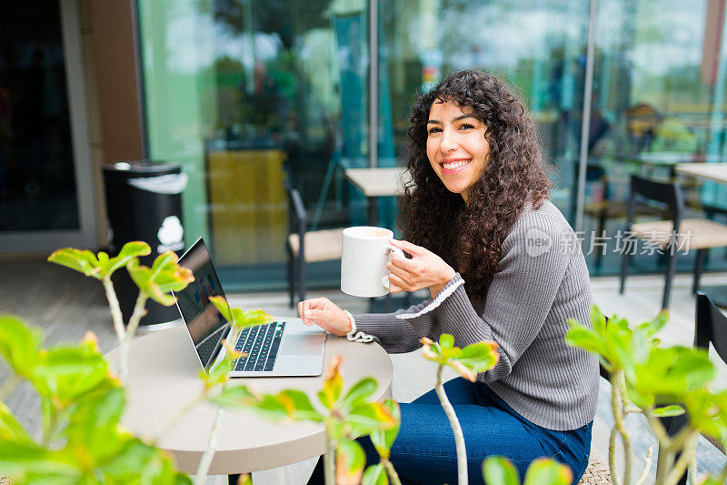迷人的女人工作在笔记本电脑喝咖啡在咖啡馆
