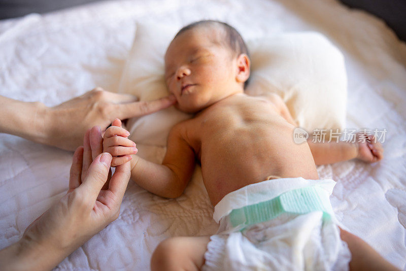 刚出生的婴儿正在睡觉，握着妈妈的手指
