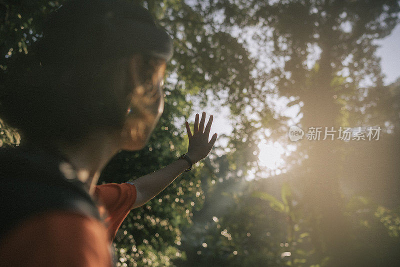 周末早晨，一名亚洲年轻女子在热带雨林徒步旅行时举手挡住阳光