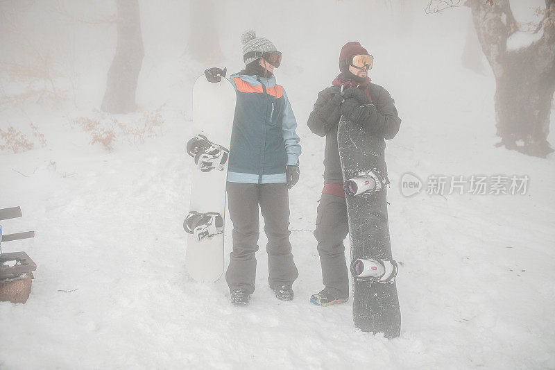 在一个雾蒙蒙的冬日，两名滑雪者站在山顶上聊天