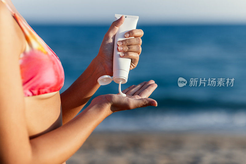 一名年轻女子在海滩上涂抹防晒霜，以保护皮肤免受阳光的伤害