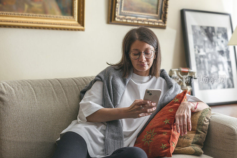 年轻的成年女子坐在客厅的沙发上玩手机