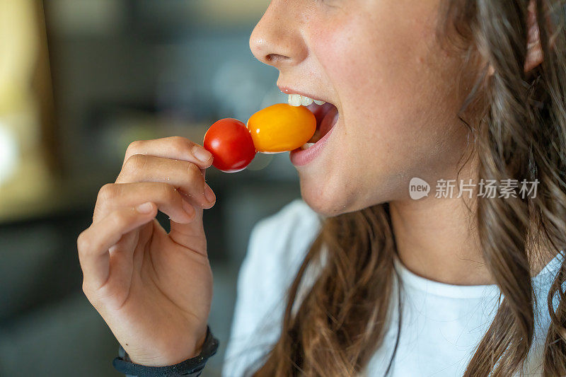 素食。一个小女孩吃着红黄相间的西红柿，细枝末节地放在嘴里