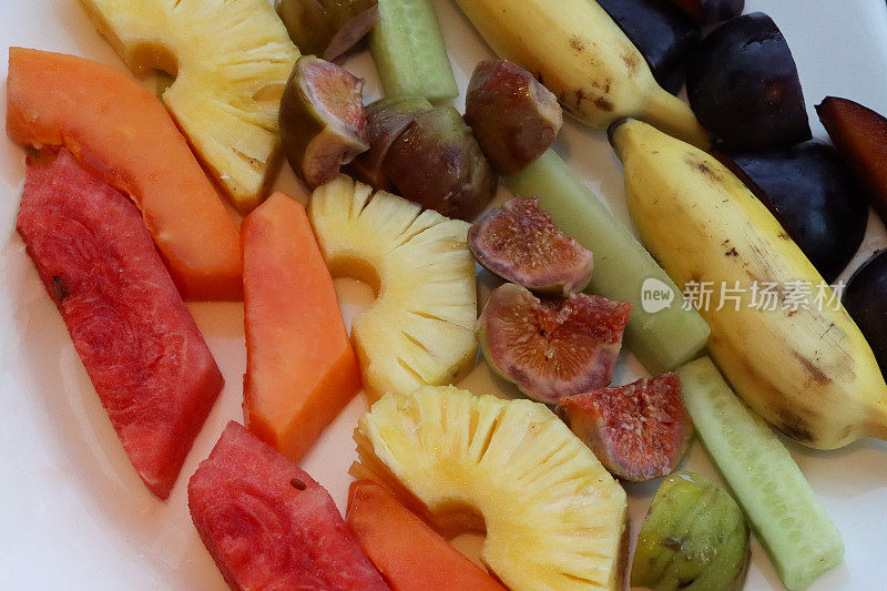 新鲜的热带水果沙拉全画幅图像，白色盘子上有一排排切片西瓜、木瓜、菠萝、无花果、瓜、香蕉和李子