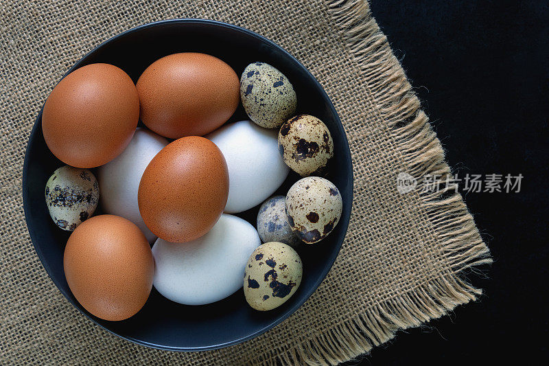 白色和棕色的鸡蛋和鹌鹑蛋在盘子里在黑色的桌子上