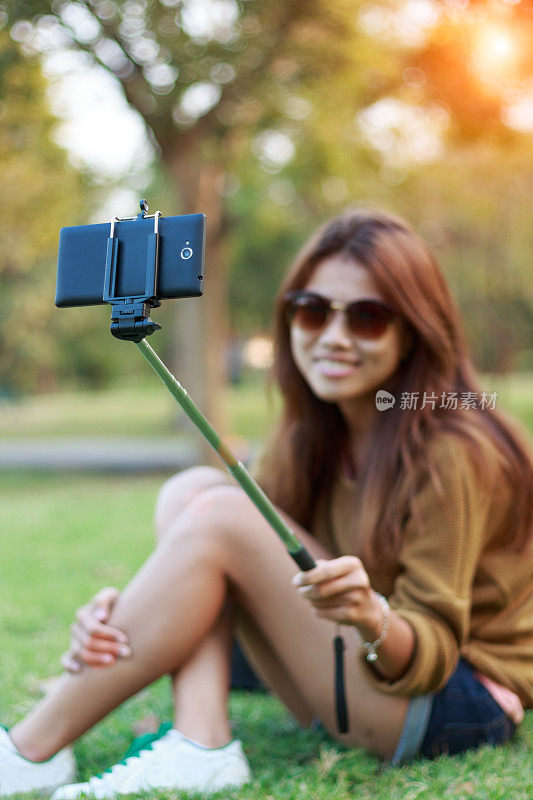 女人拿着单脚架用智能手机自拍拍照