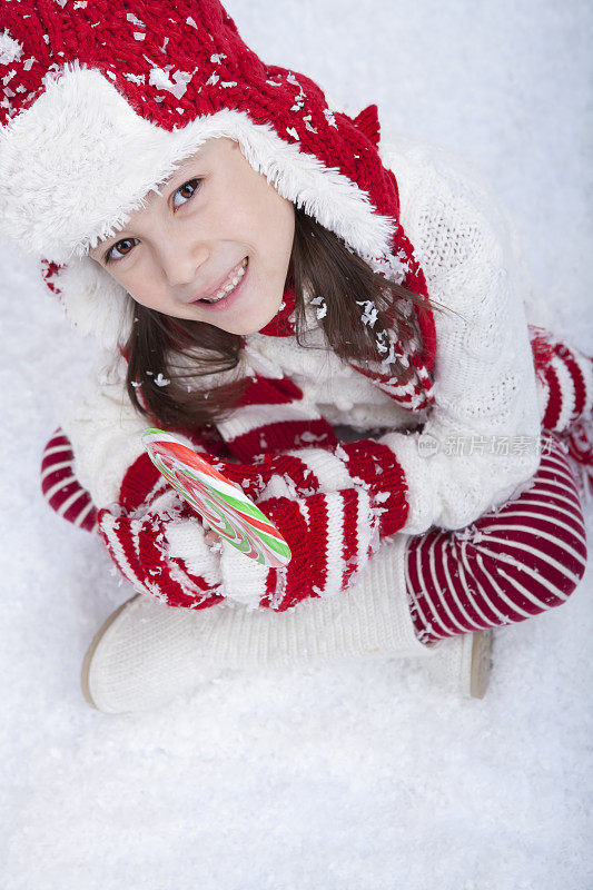 小女孩坐在雪地里，手里拿着糖果