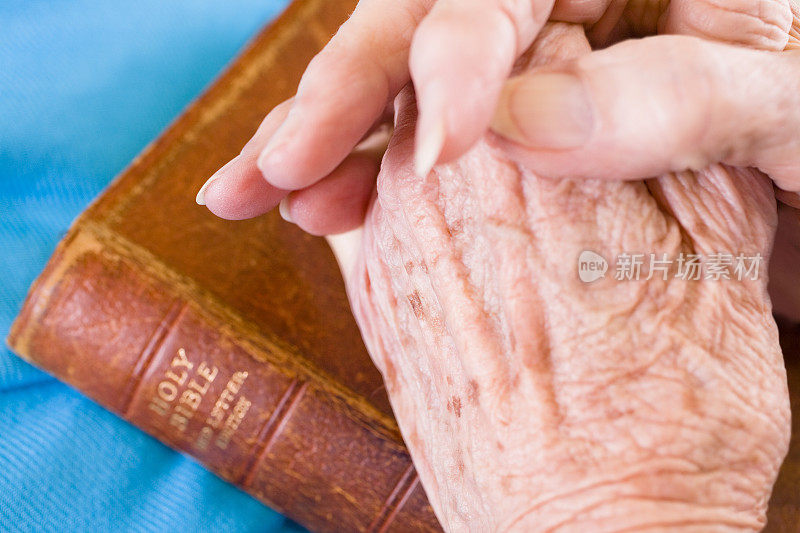 年长的成年妇女双手合十在圣经祈祷。