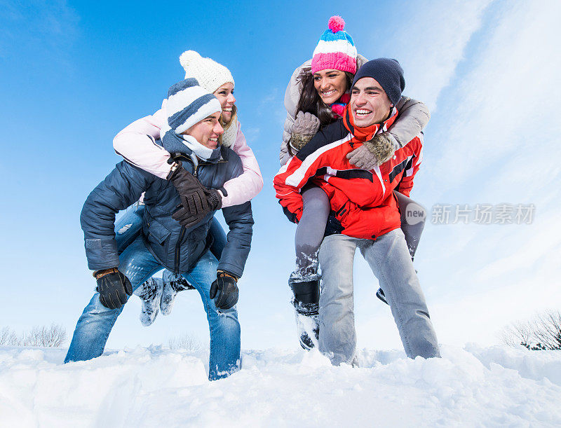 微笑的男人背着他们的女朋友在雪地上。