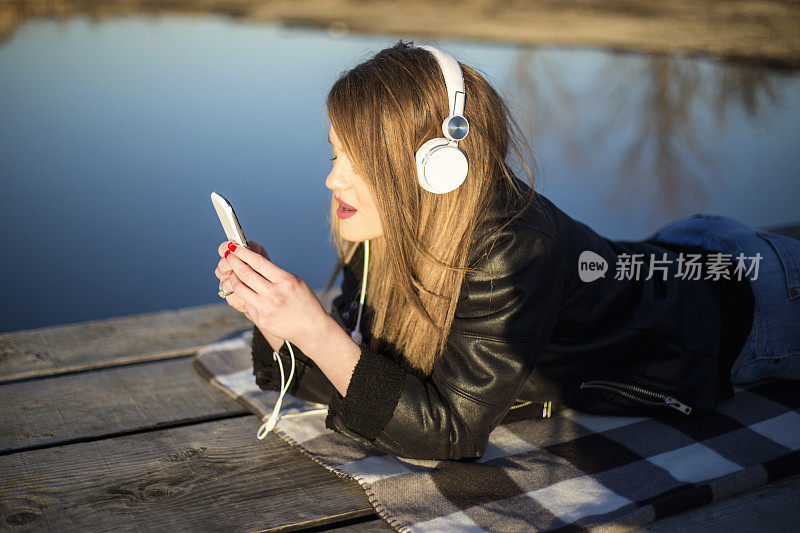 戴着耳机的女人在湖边码头上听音乐