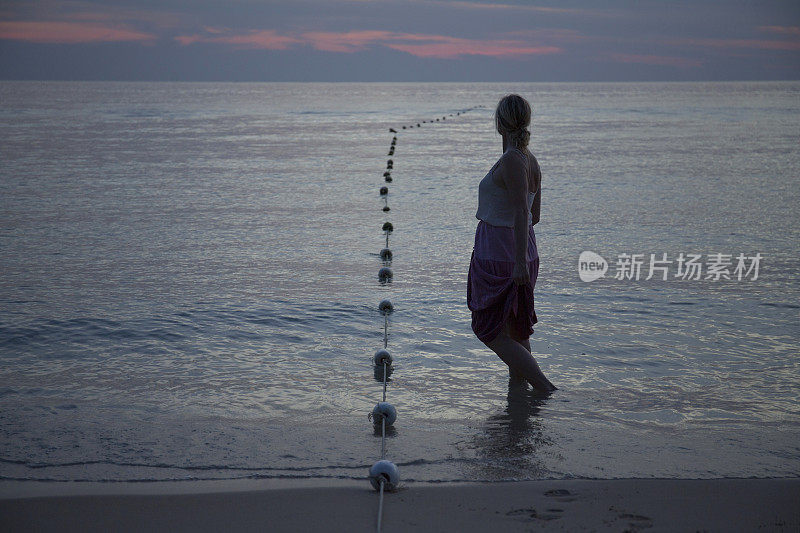 黄昏时分，一名女子在海滩上驻足观赏大海