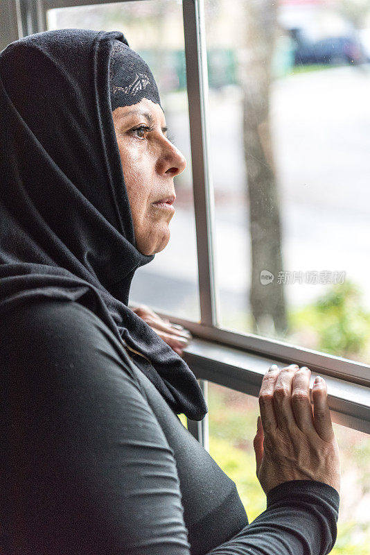 关切的穆斯林妇女透过窗户看