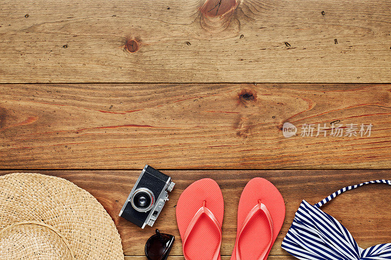 平铺的太阳帽，照相机，人字拖和比基尼在木头上