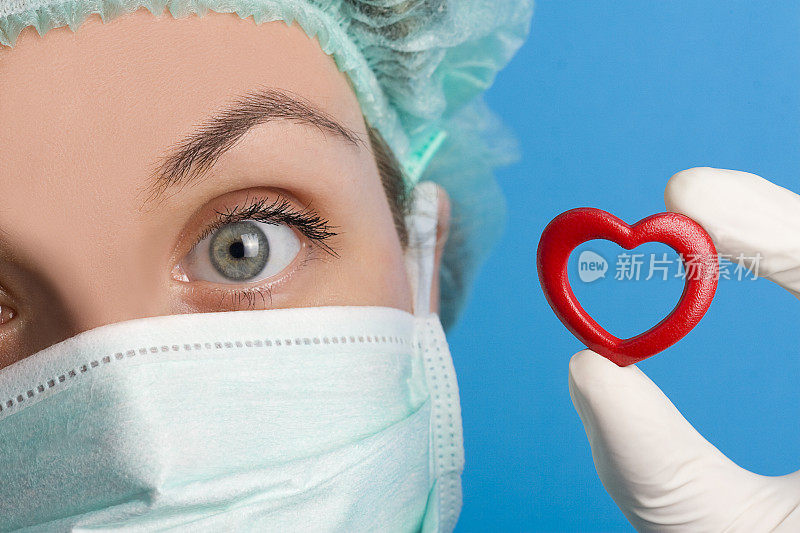 一个戴面具的医生拿着一个红色的心脏形状的特写图像