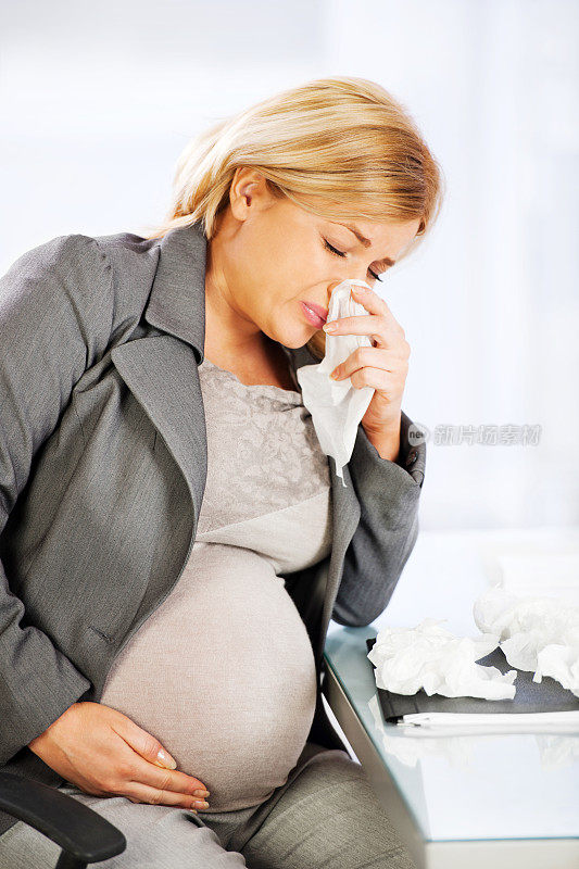 年轻怀孕的女商人正在擤鼻涕。