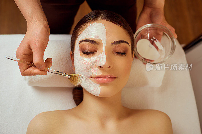 在脸部的女性美容师应用面膜在水疗沙龙
