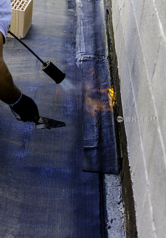 屋顶工人安装卷筒沥青防水膜，用于防水平台