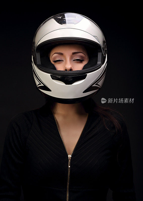美丽性感的化妆女人看在白色摩托车头盔上的黑色背景。黑暗特写肖像