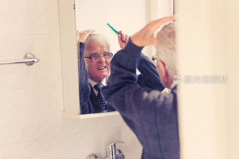 老年人在家里。老男人看着浴室的镜子，整理着他的头发