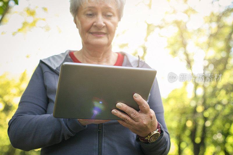 开朗的老年妇女在运动服装后使用数码平板电脑。专注在手边。