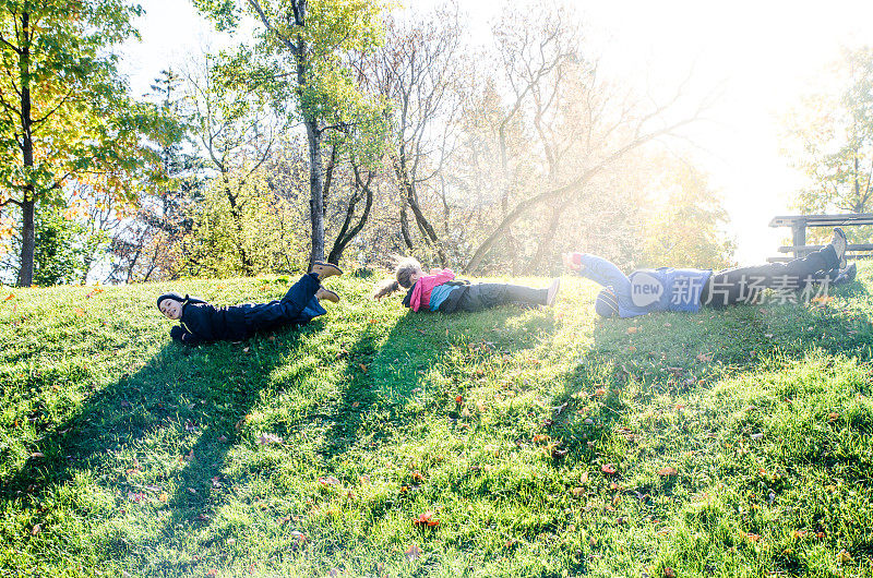 母亲，儿子和女儿在一个公园的草山上滚动在秋天的一天