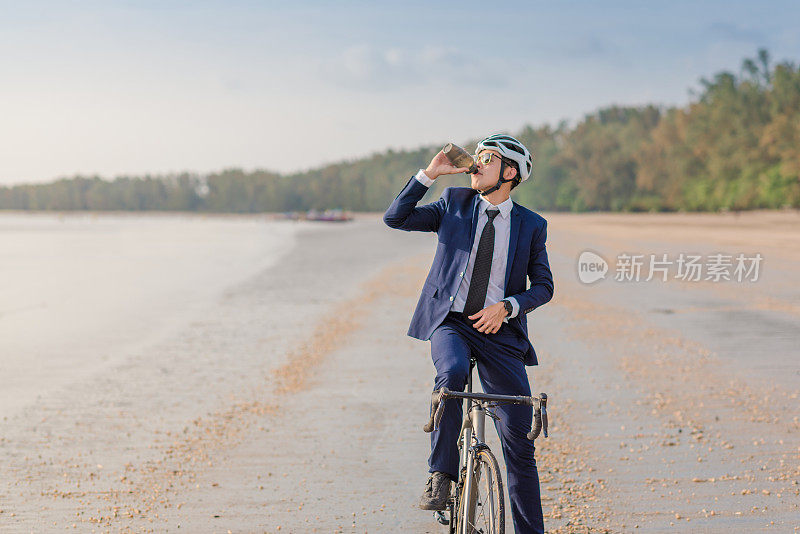 年轻的亚洲商人骑自行车放松海滩日落