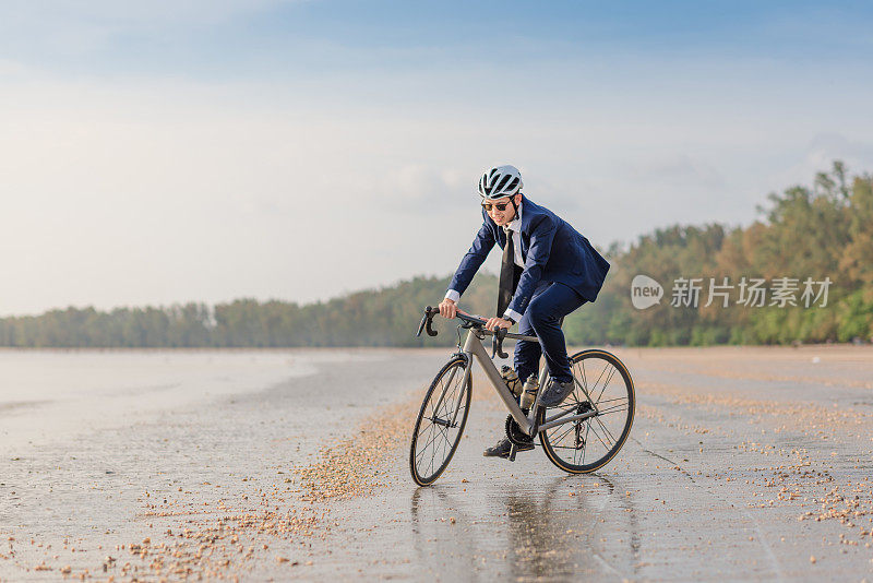 年轻的亚洲商人骑自行车放松海滩日落