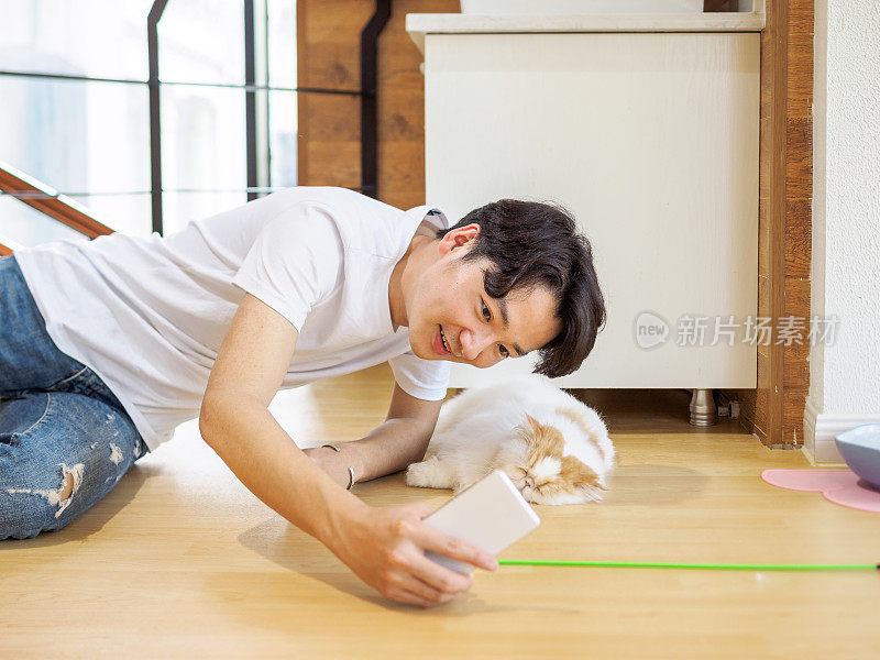 英俊的中国青年在家与一只慵懒的毛绒绒的猫自拍。