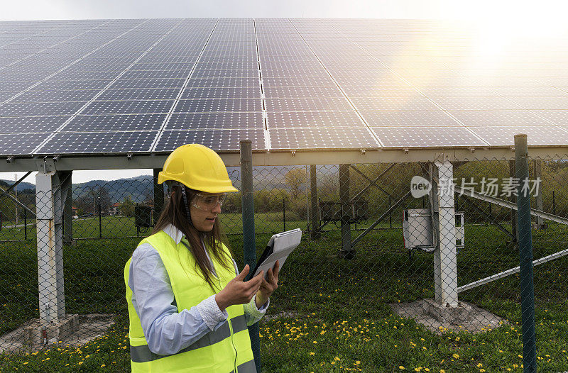 太阳能电池板。电力工程师在太阳能发电站附近的田野工作，晴朗的蓝天和阳光在他们的身后。