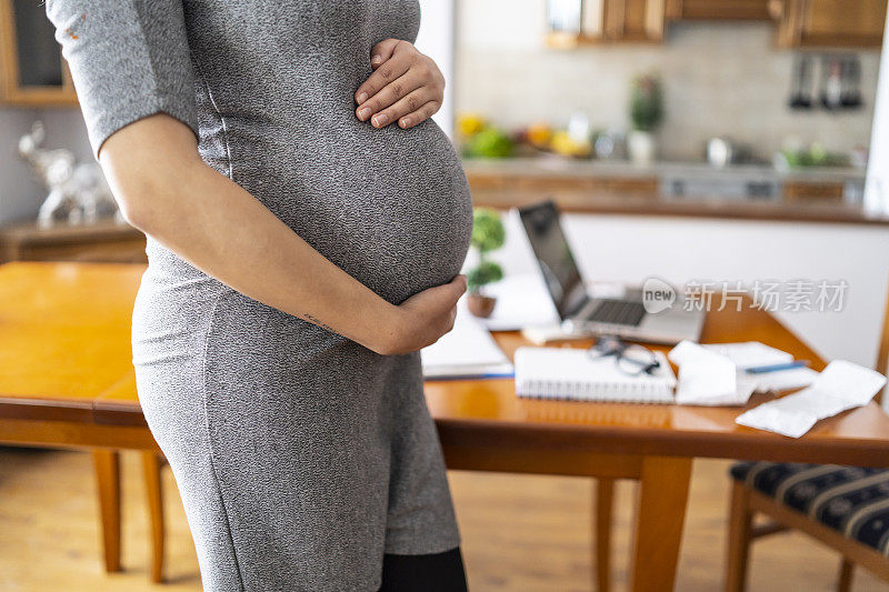 孕妇站在家里，手放在肚子上