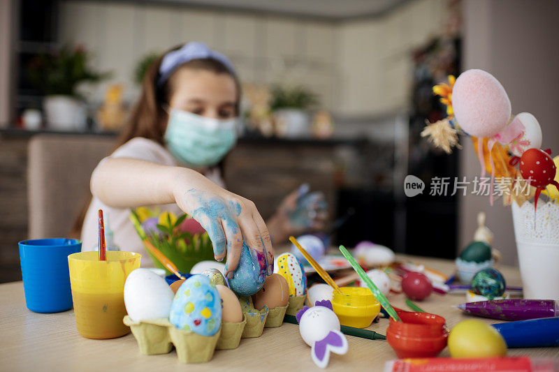 女孩用防护面具画复活节彩蛋。病毒防护的概念。库存图片