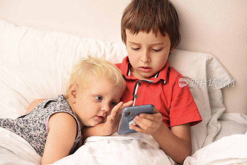 孩子们在床上用智能手机看电影。