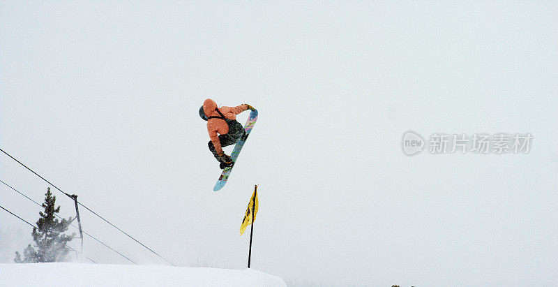 在科罗拉多州博尔德附近的埃尔多拉滑雪度假村，一个滑雪板在一个下雪的，阴天试图在一个跳跃上“正面360尾抓”把戏