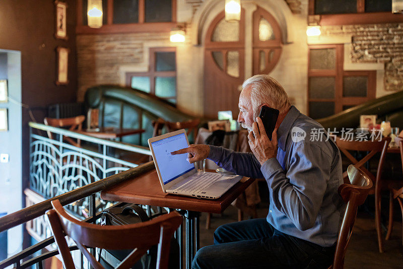 现代成熟的商人在咖啡馆打电话和使用笔记本电脑