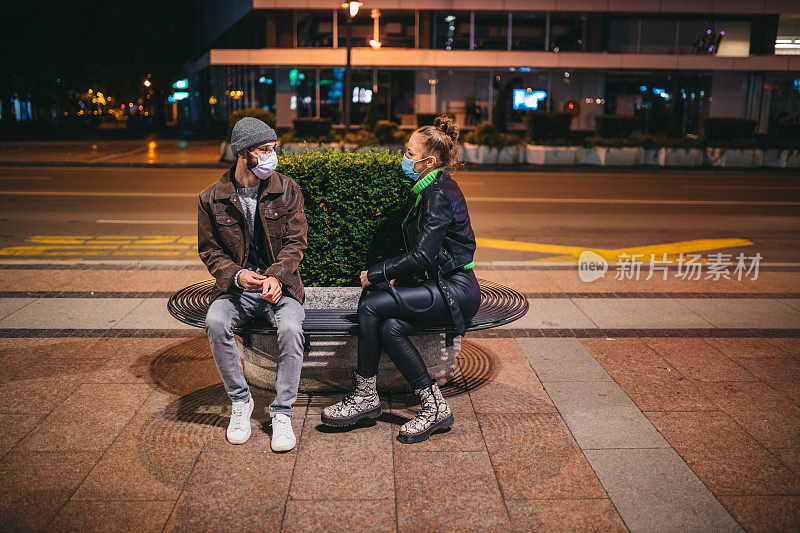 年轻的白人朋友们戴着N-95面具在汽车站边聊天边等车