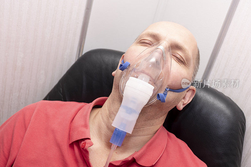 一个40到50岁的白人男性，用喷雾器吸入。人像，男人的眼睛是闭着的。