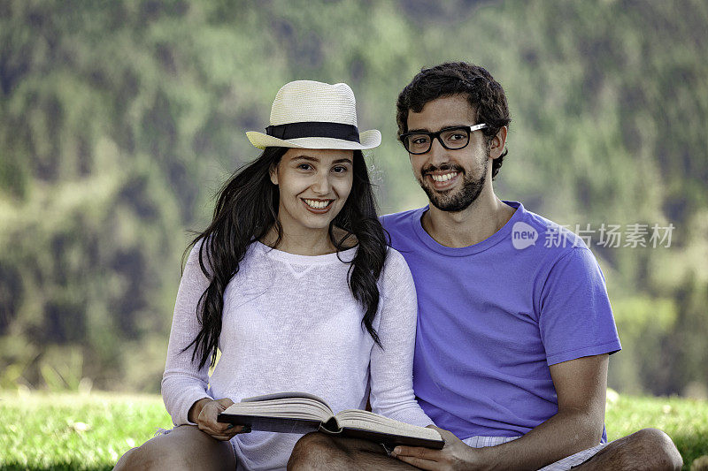 年轻的西班牙夫妇在草地上看书。野餐时间。