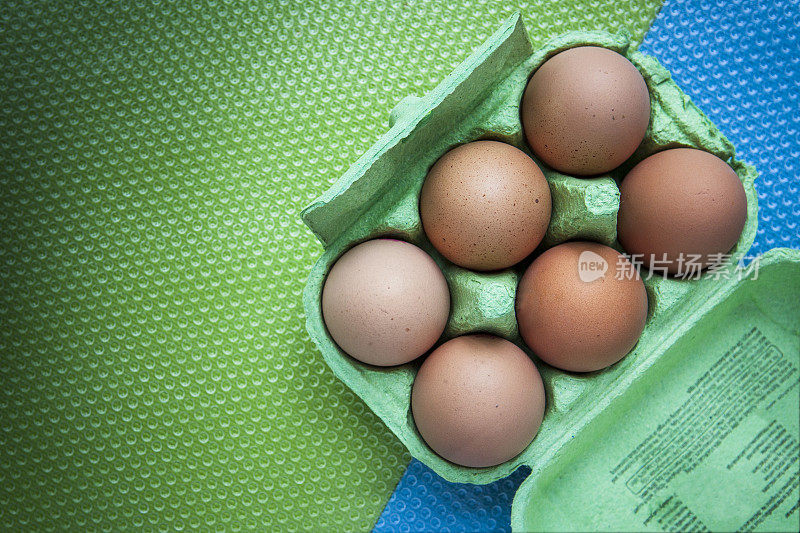 6个鸡蛋放在一个绿色的硬纸板鸡蛋盒里，上面有一个绿色和蓝色的塑料凹纹表面
