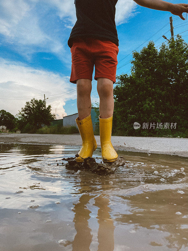 穿着黄色胶靴在水坑里跳跃的孩子，快乐的童年