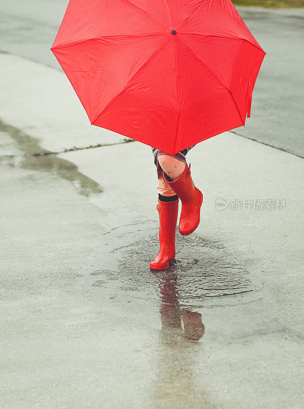 无名的孩子雨靴和伞在雨天的水坑里溅起水花