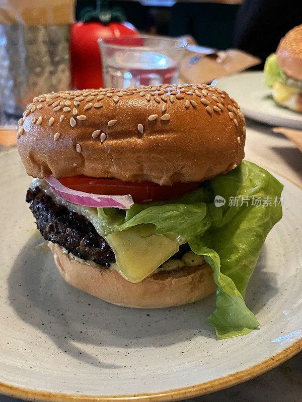 餐桌上摆放着芝麻饼、融化的奶酪、西红柿、红洋葱片和生菜叶，白色盘子，一杯饮用水的餐厅场景形象，聚焦前景