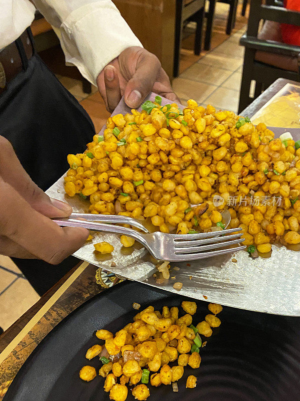 在印度餐厅用叉子和勺子在餐桌上供应鹰嘴豆咖喱的不知名的服务员的图像，用餐外的地方设置餐服务，重点在前景