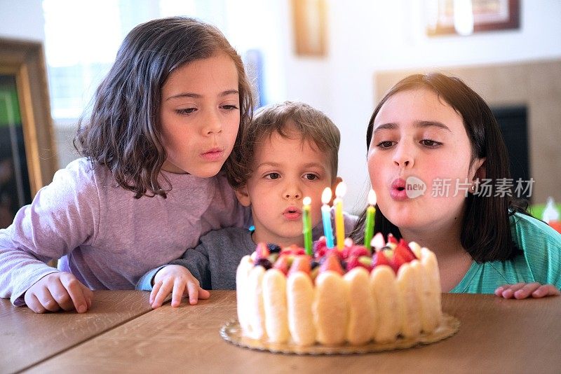 孩子们吹着生日蛋糕蜡烛庆祝生日