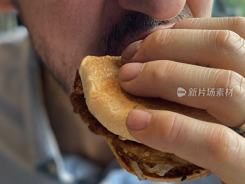全帧图像的白人男子咬汉堡在一个圆面包，集中在前景
