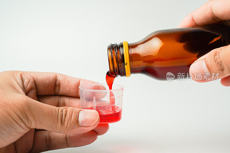 健康理念，人与药的理念——将药瓶或解热糖浆倒入药杯、药勺中，孤立的白色背景